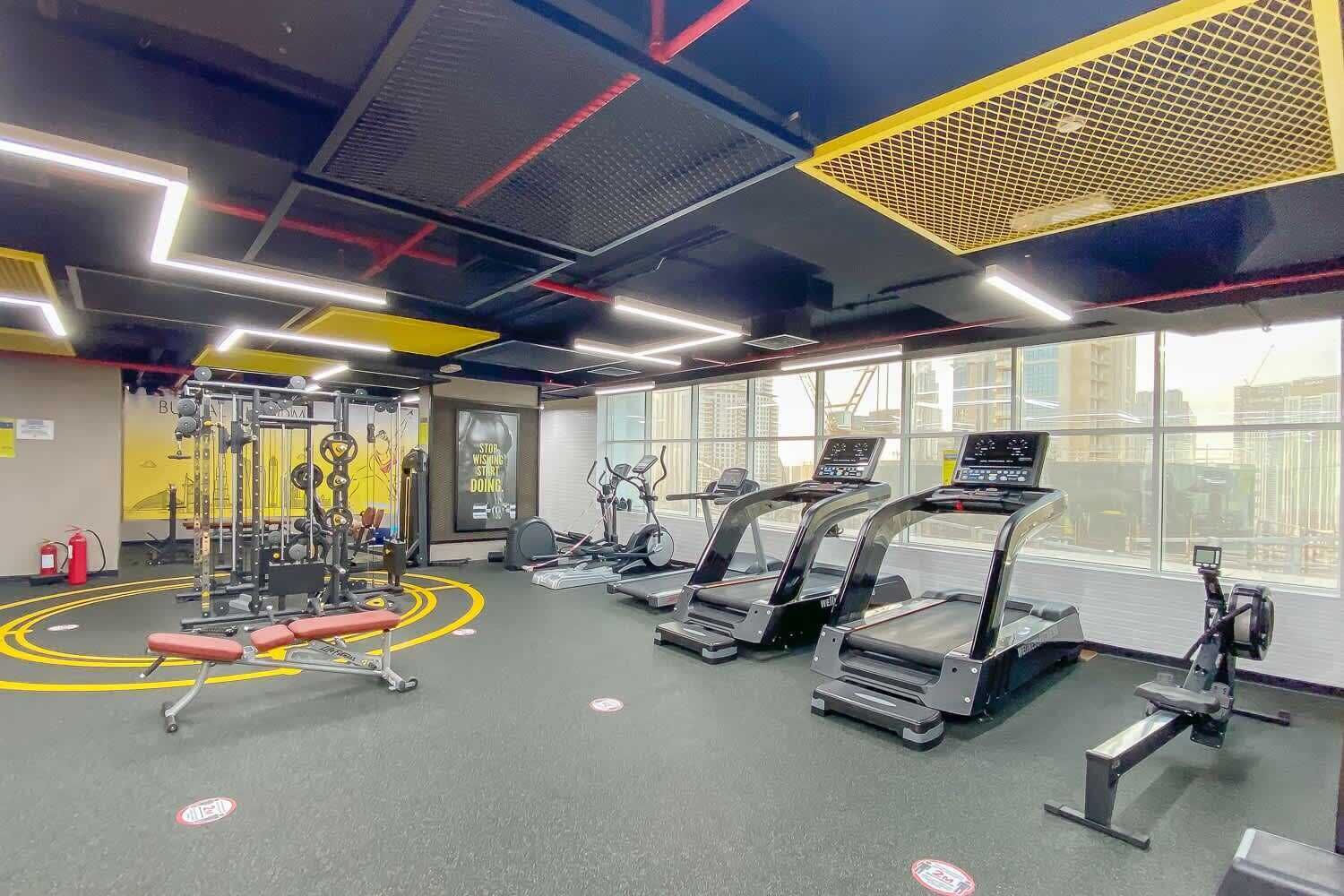 A gym with treadmills, weight machines, and a red bench.