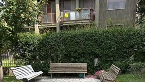A paved pathway leading to a wooden bench surrounded by greenery, with a building in the background. - Cosy Studio Quick Metro Ride to Centre (Milan)