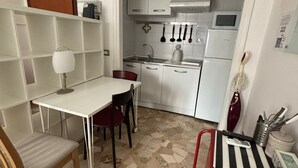 A compact kitchen with white cabinets, a microwave, and a sink. There is a dining table with chairs and a small red chair. - Cosy Studio Quick Metro Ride to Centre (Milan)