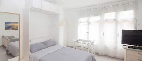 A bedroom with a bed, bedside tables, a desk, a TV, and a window with curtains.