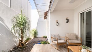 Een klein terras met houten vloer, een plant in pot, een rieten stoel en een tafel.
