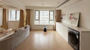 Une cuisine moderne équipée d’un lave-linge intégré, un coin repas avec un canapé et de grandes fenêtres offrant une vue sur la ville.