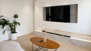 A modern living room with a large TV mounted on the wall, a wooden coffee table, and a potted plant.