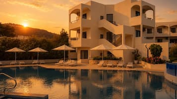 A modern hotel with a pool, sun loungers, and umbrellas.