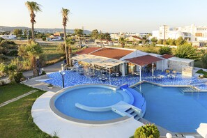 A pool area with a circular pool, outdoor seating, and a building with a red-tiled roof. - Rhodea Mar (Rhodes)