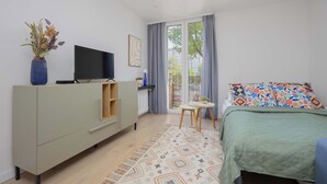 Un dormitorio moderno con una cama, un televisor sobre un mueble, una mesita y vistas al exterior.