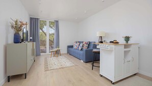 Una sala de estar moderna con un sofá, una mesita, un armario y una cocina con encimera y electrodomésticos.