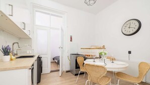 Una cocina moderna con armarios blancos, lavavajillas integrado y un comedor con sillas de mimbre y una mesa blanca.