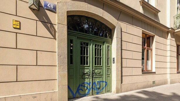 Un edificio con una puerta verde, un cartel con el número 28 y una ventana con una reja de metal.