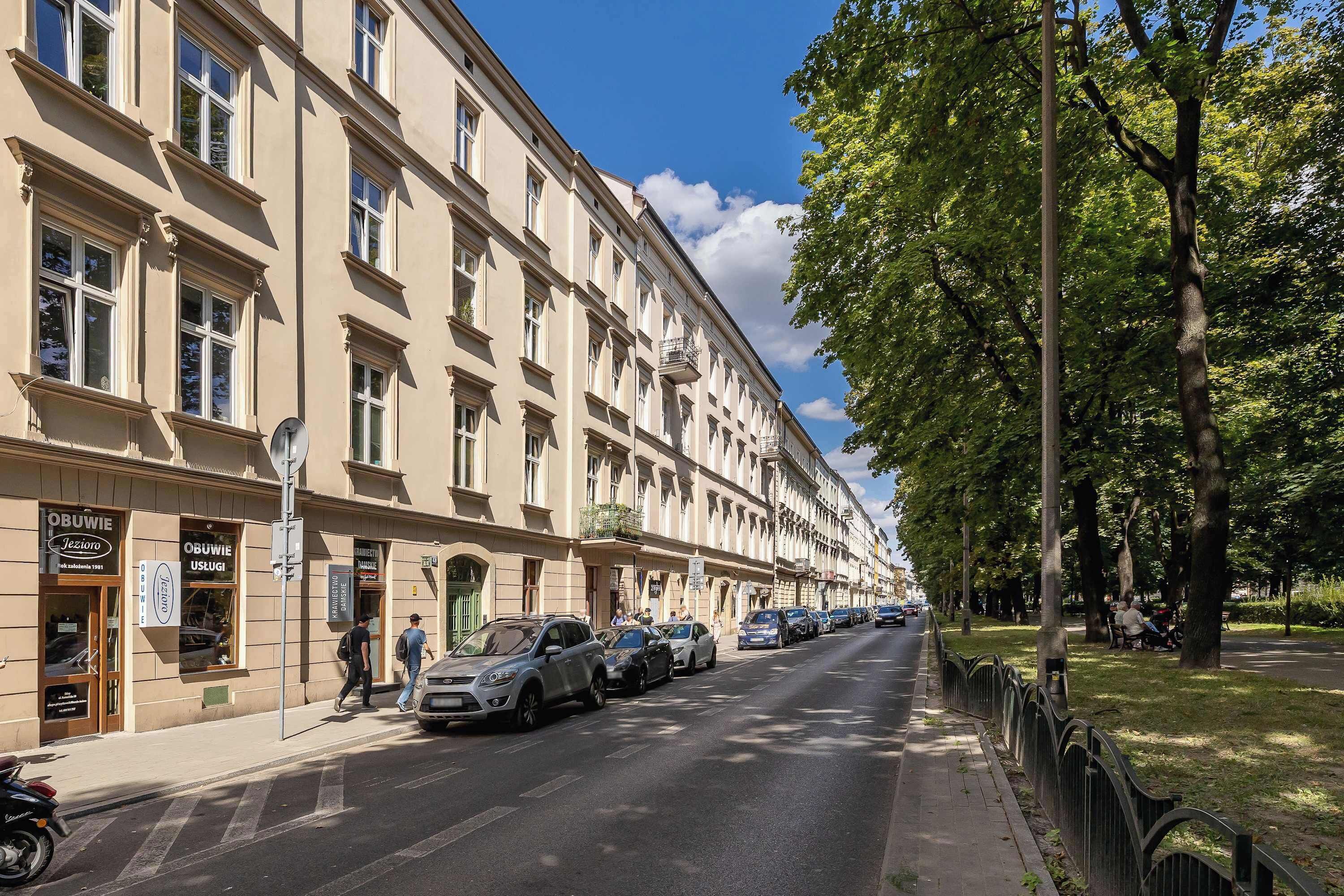 Eine Straße mit parkenden Autos und einem Gebäude mit zahlreichen Fenstern und Balkonen.