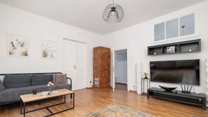 Una sala de estar moderna con un sofá gris, una mesa de centro de madera y un televisor grande sobre un soporte negro.