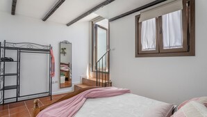 Een slaapkamer met een bed, een raam met gordijnen, een houten trap en een metalen garderobe.