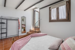 Ein Schlafzimmer mit einem Bett, einem Fenster mit Vorhängen, einer Holztreppe und einem Metallschrank.