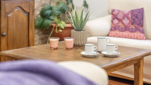 Een houten tafel met vier kopjes en schotels, een potplant en een bank met een gekussend kussen in een knusse kamer.