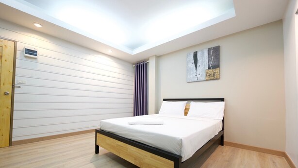 A modern bedroom with a skylight, a bed with white linens, a wooden floor, and a painting on the wall. - Little Rooms (Chanthaburi)