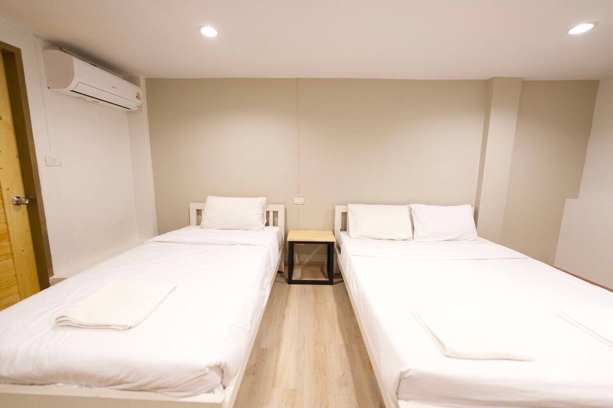 Ein Hotelzimmer mit zwei Einzelbetten, einer Holztür, einer Klimaanlage und einem kleinen Nachttisch.