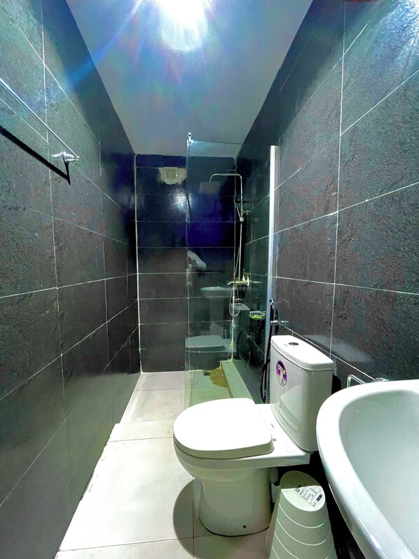 A small, modern bathroom with dark tiles, a toilet, a shower, and a bathtub.