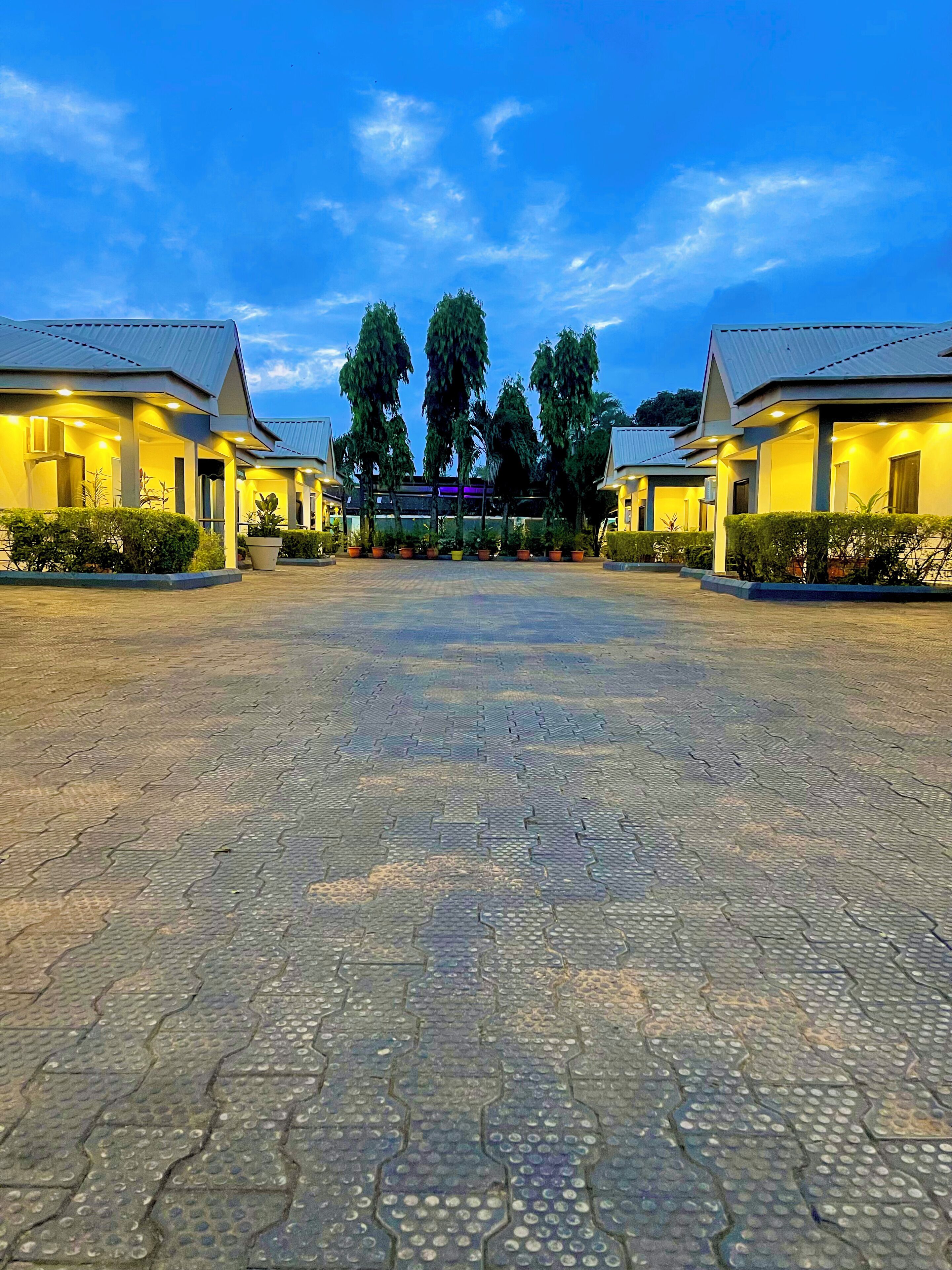 A hotel with a paved courtyard, two-story buildings, and a central entrance with trees.