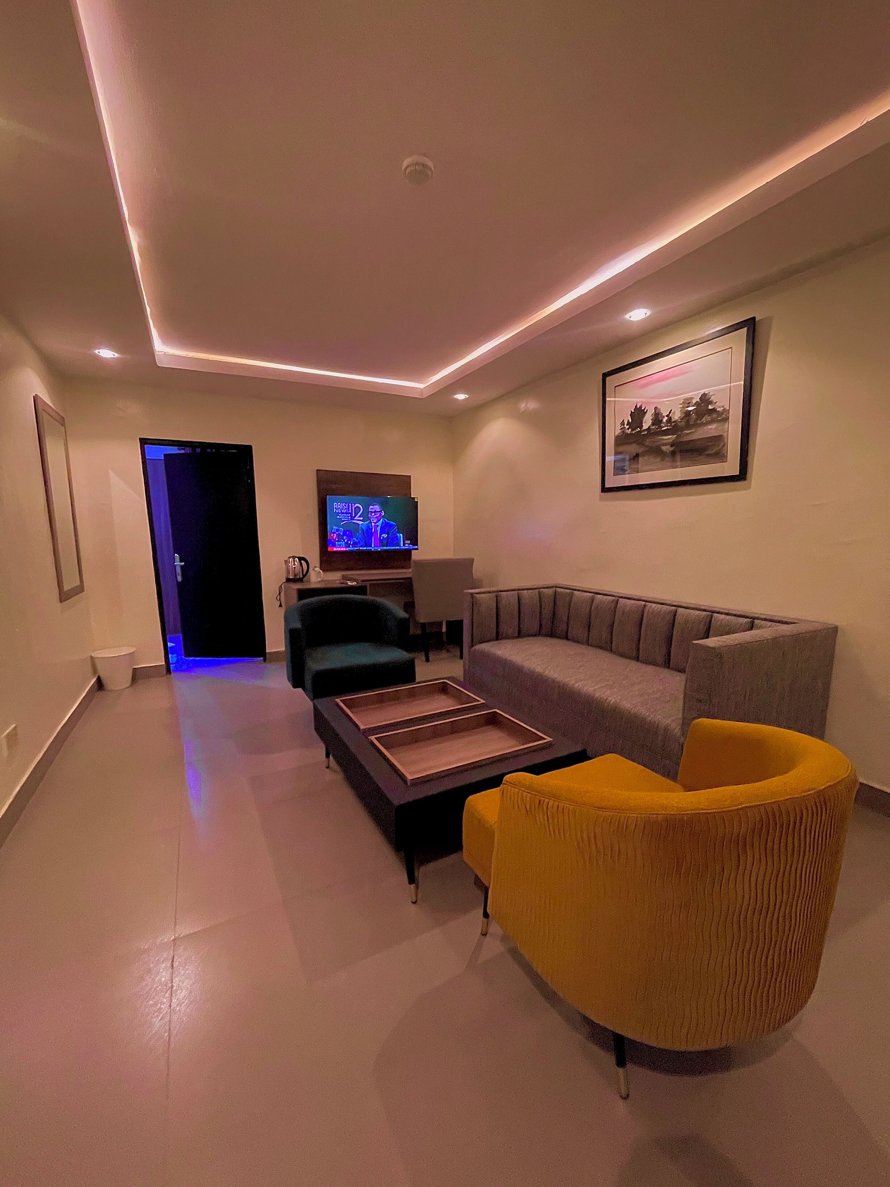 Een moderne woonkamer met een grijze bank, een gele fauteuil, een houten salontafel en een televisie aan de muur.