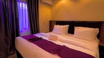 A hotel room with a large bed, a ceiling-mounted air conditioner, and a window with purple lighting.