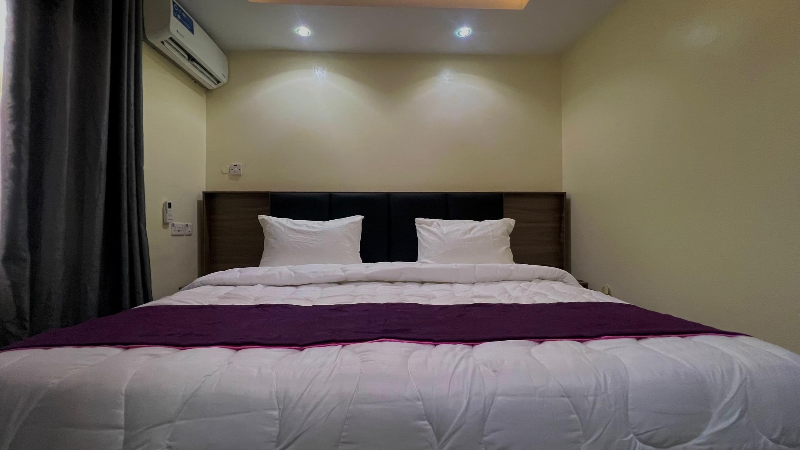 Een hotelkamer met een bed, hoofdeinde, een ingebouwde airconditioning en een plafondlamp.