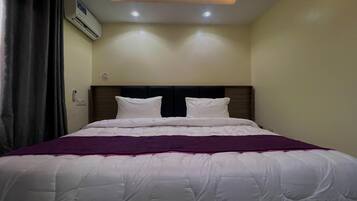 Een hotelkamer met een bed, hoofdeinde, een ingebouwde airconditioning en een plafondlamp.
