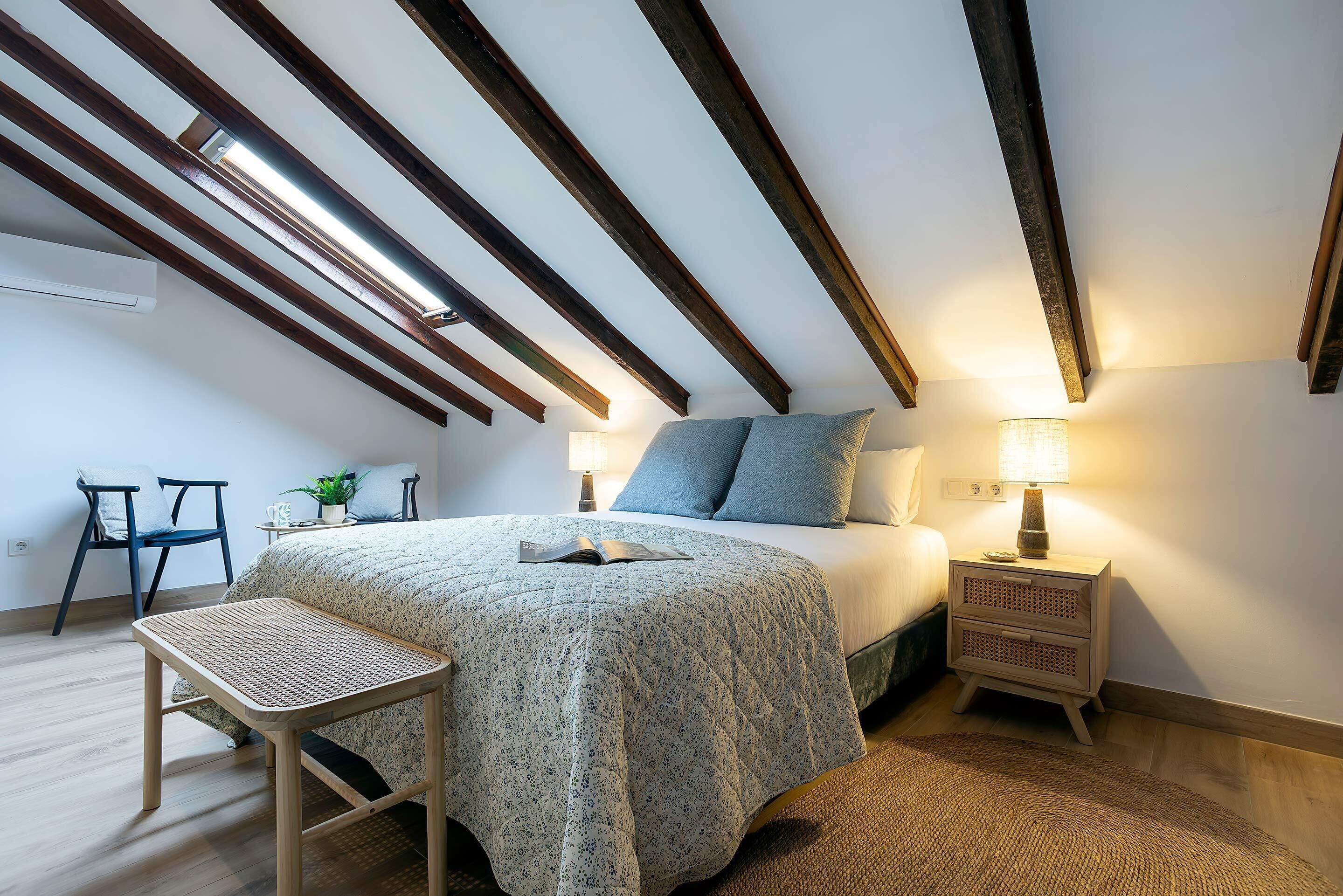 Un dormitorio con cama, mesita de noche, lámpara y una pequeña mesa con una silla.