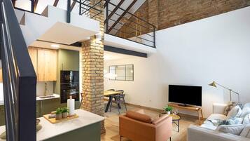 Ein modernes Loft mit Küche, Essbereich und Wohnzimmer, das unverputzte Backsteinwände, Holzbalken und einen großen Fernseher zeigt.