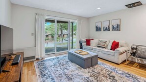 A modern living room with a sofa, ottoman, and a flat-screen TV. - Condo with Fireplace & Pool, Deere Run (Quechee)