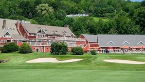 A red building with multiple windows and a balcony, surrounded by green grass and trees. - Condo with Fireplace & Pool, Deere Run (Quechee)