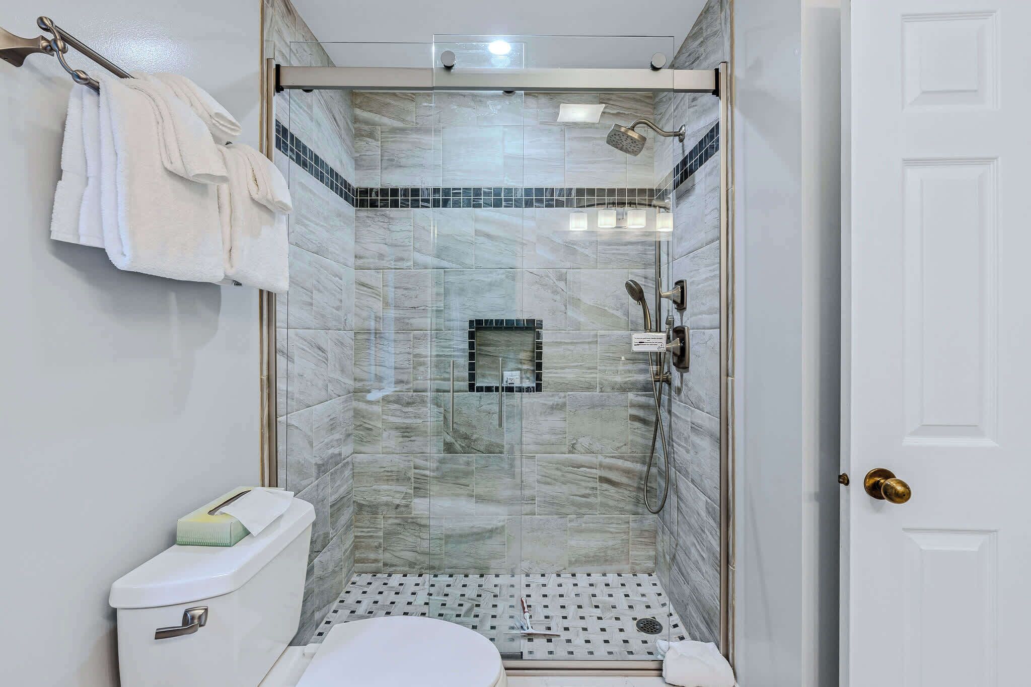 A walk-in shower with a glass door, a toilet, and a towel rack with towels.