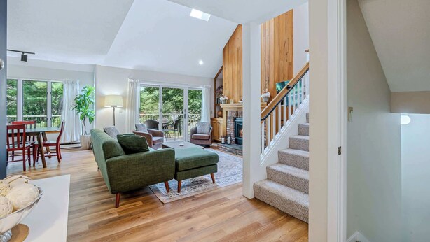 A spacious living room with a green sofa, wooden flooring, and a staircase leading to an upper level. - Condo with Fireplace & Pool, Deere Run (Quechee)