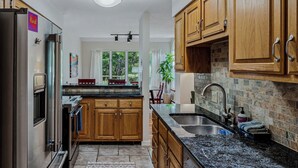 A modern kitchen with granite countertops, wooden cabinets, and a built-in dishwasher. - Condo with Fireplace & Pool, Deere Run (Quechee)