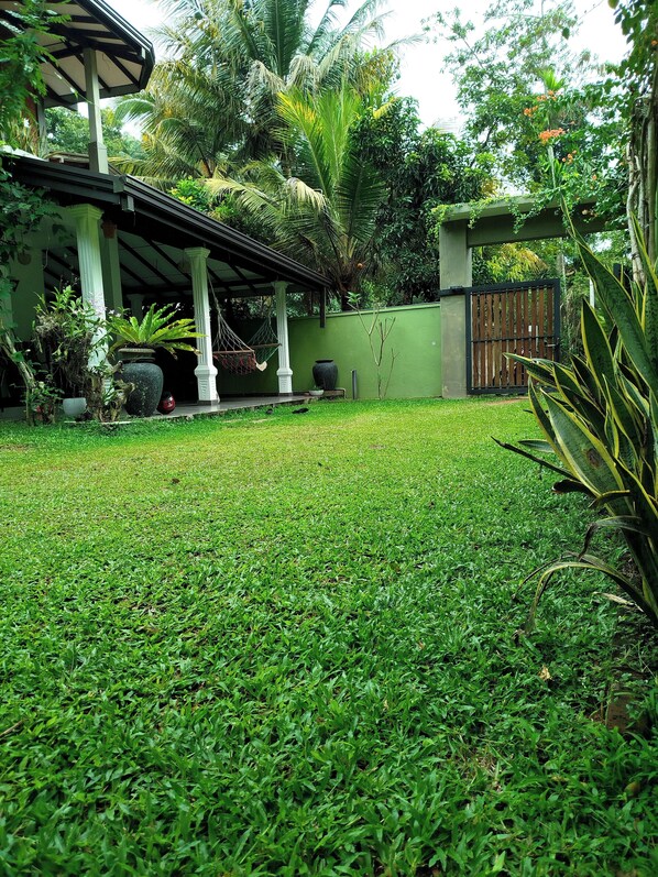 Un jardín bien cuidado con un pabellón, diversas plantas y una entrada protegida por una reja.