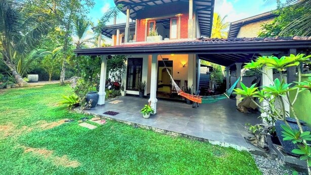 A two-story house with a covered porch, a hammock, and a well-maintained garden.