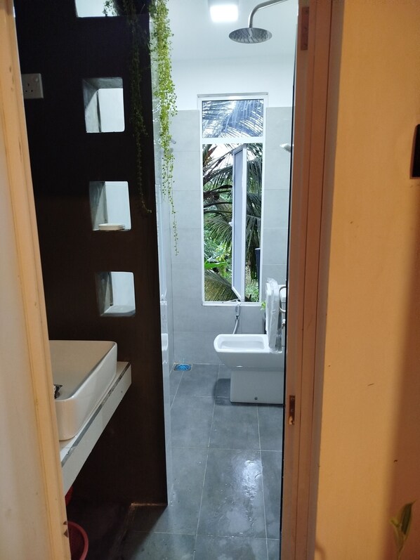 Un baño con ducha, lavamanos y ventana con vistas a zonas verdes.