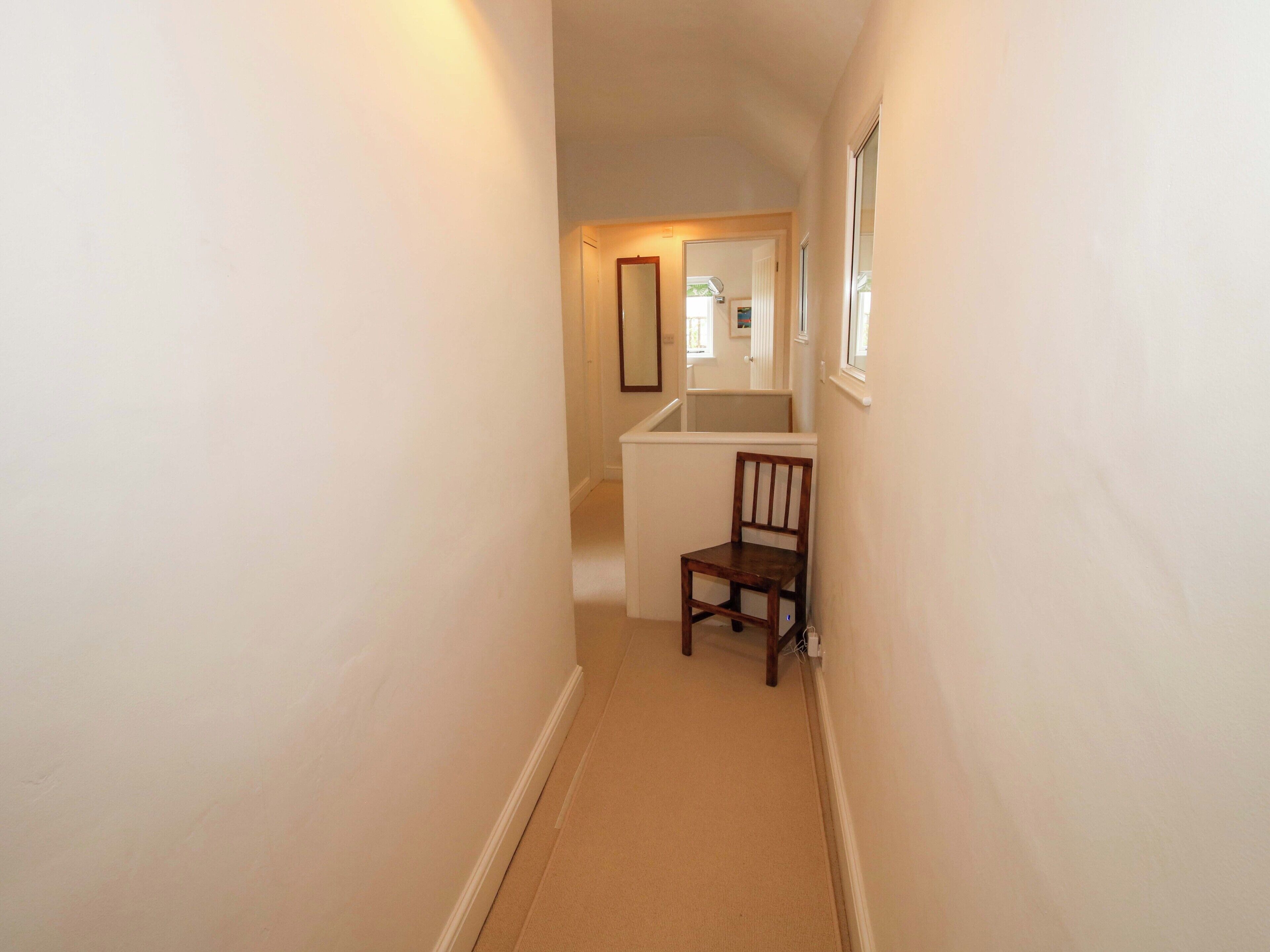 A narrow hallway with a wooden chair and a door leading to a room.