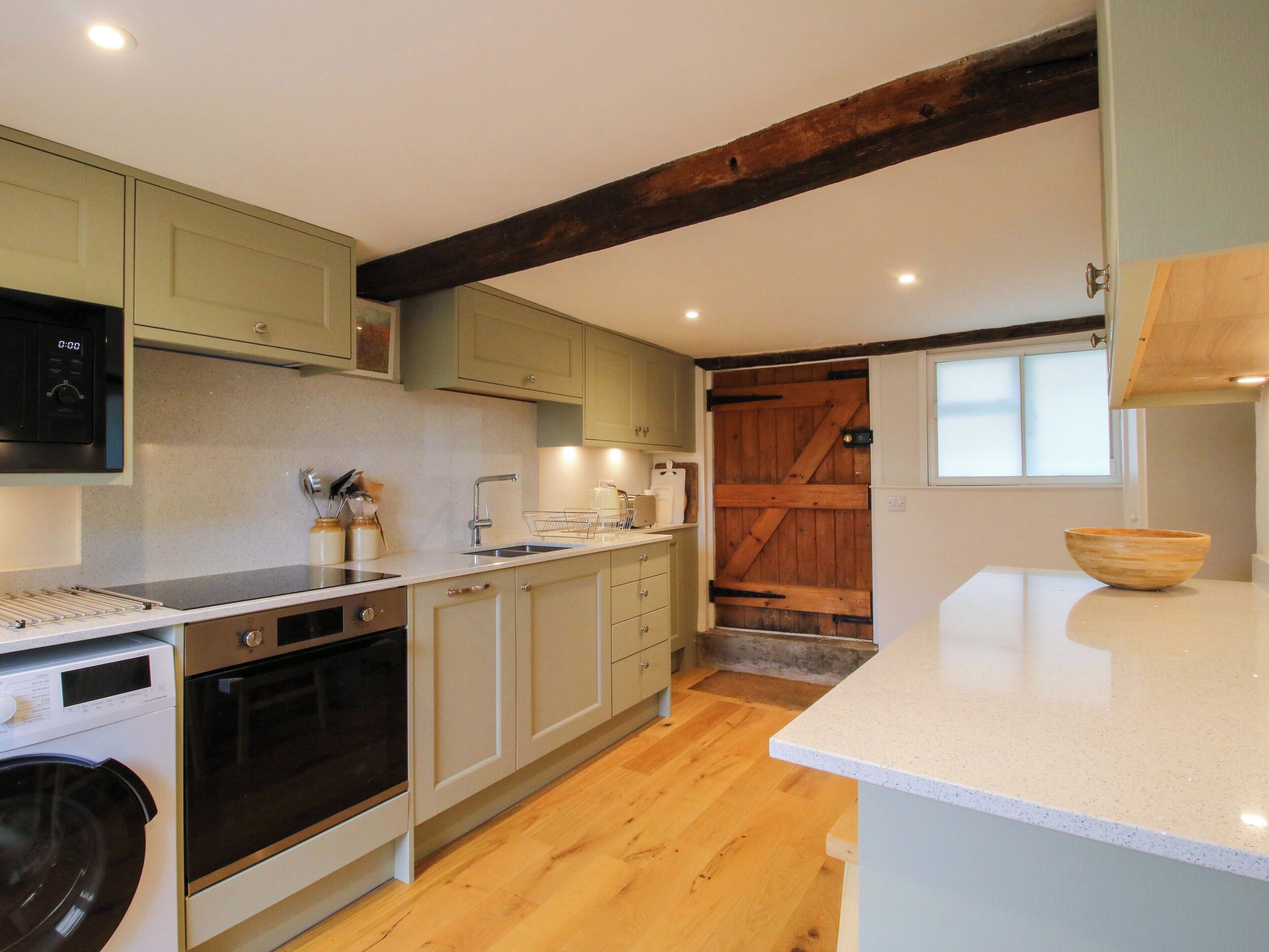 A kitchen with wooden beams, a washing machine, a microwave, and a wooden door.
