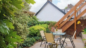 Eine Terrasse mit Tisch und Stühlen, umgeben von üppiger Bepflanzung und einer Ziegelmauer.