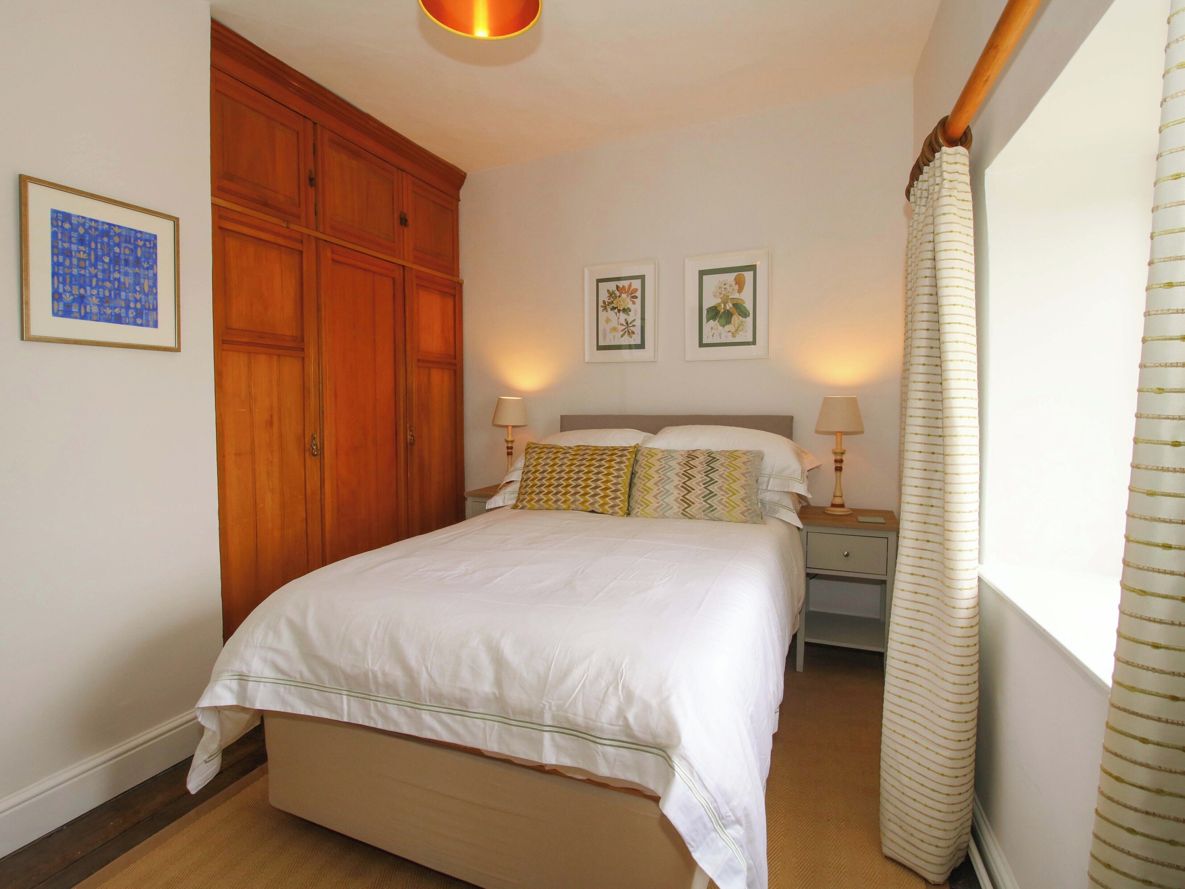Una camera da letto con un letto grande, un'armadioa in legno, due lampade ai comodini e quadri appesi al muro.
