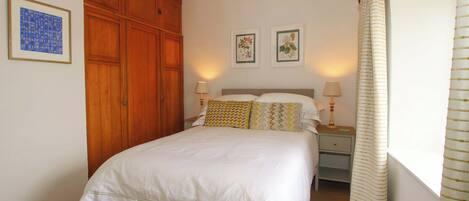 A bedroom with a large bed, wooden wardrobe, two bedside lamps, and framed pictures on the wall.