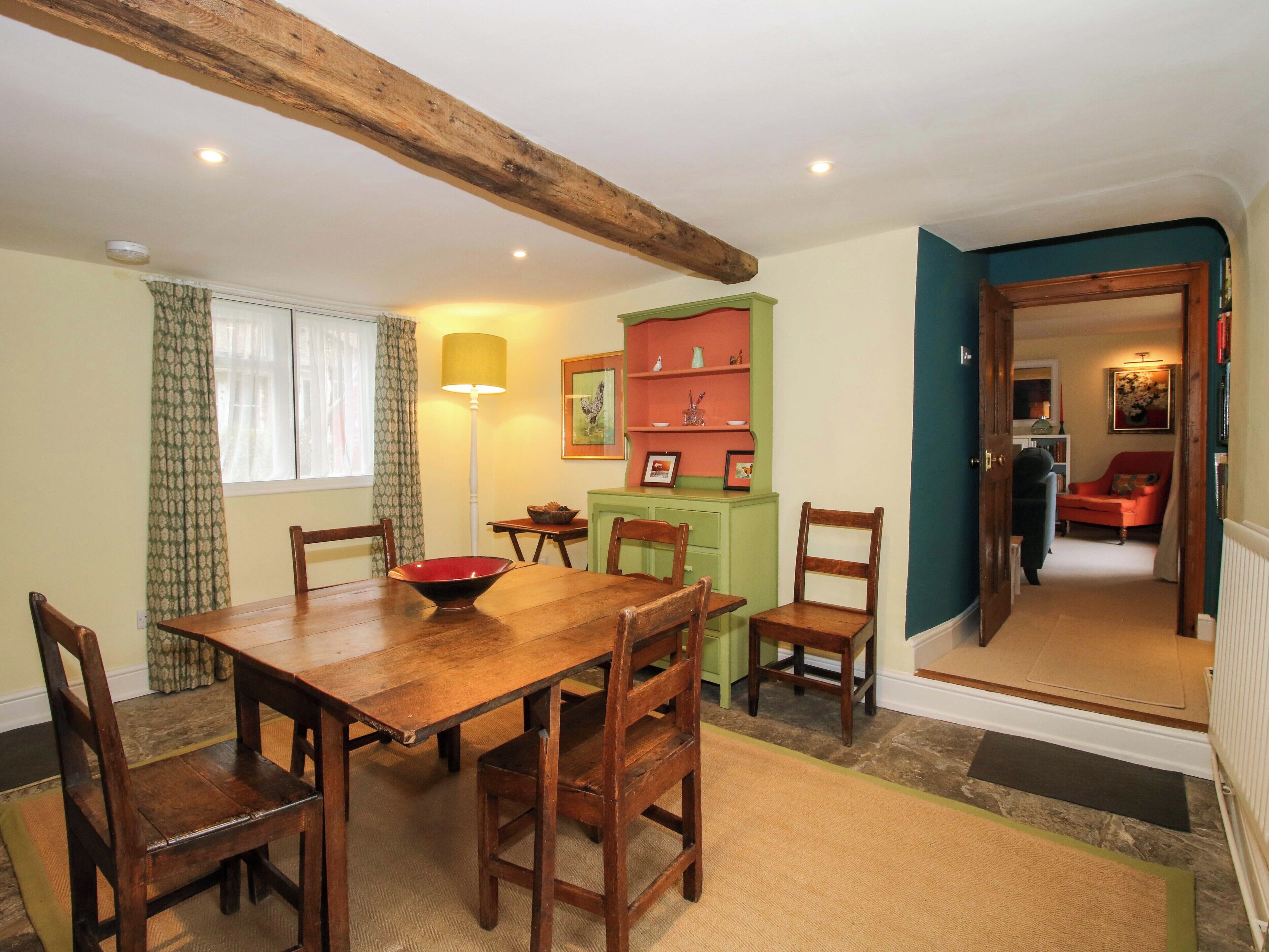 A dining area with a wooden table and chairs, a green cabinet with decorative items, and a red chair in the background.
