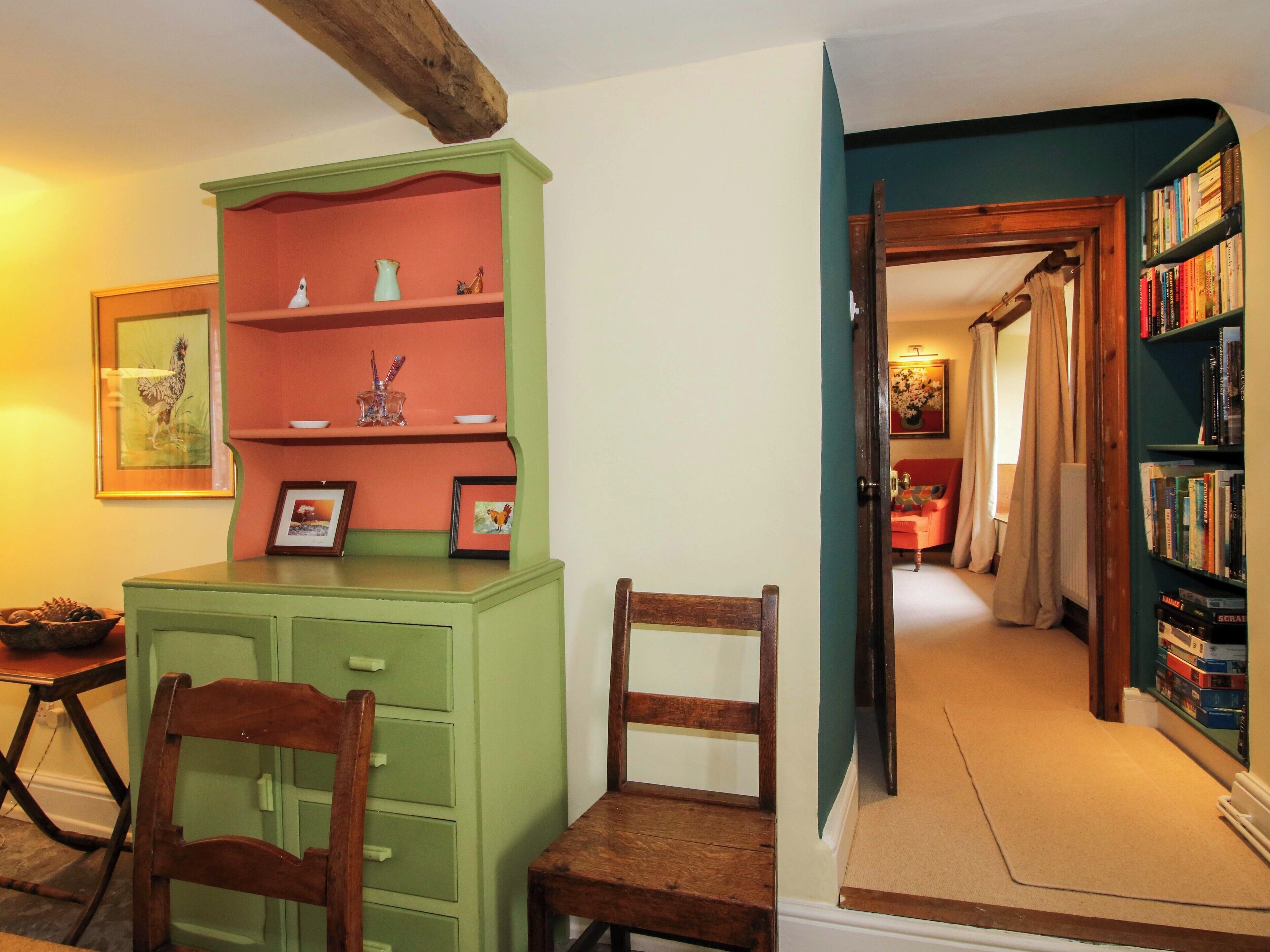 Une pièce avec un meuble vert, une chaise en bois, une bibliothèque et un tableau encadré au mur.