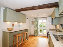 A kitchen with wooden stools, a wooden bowl on the counter, and a view of the garden through the door.