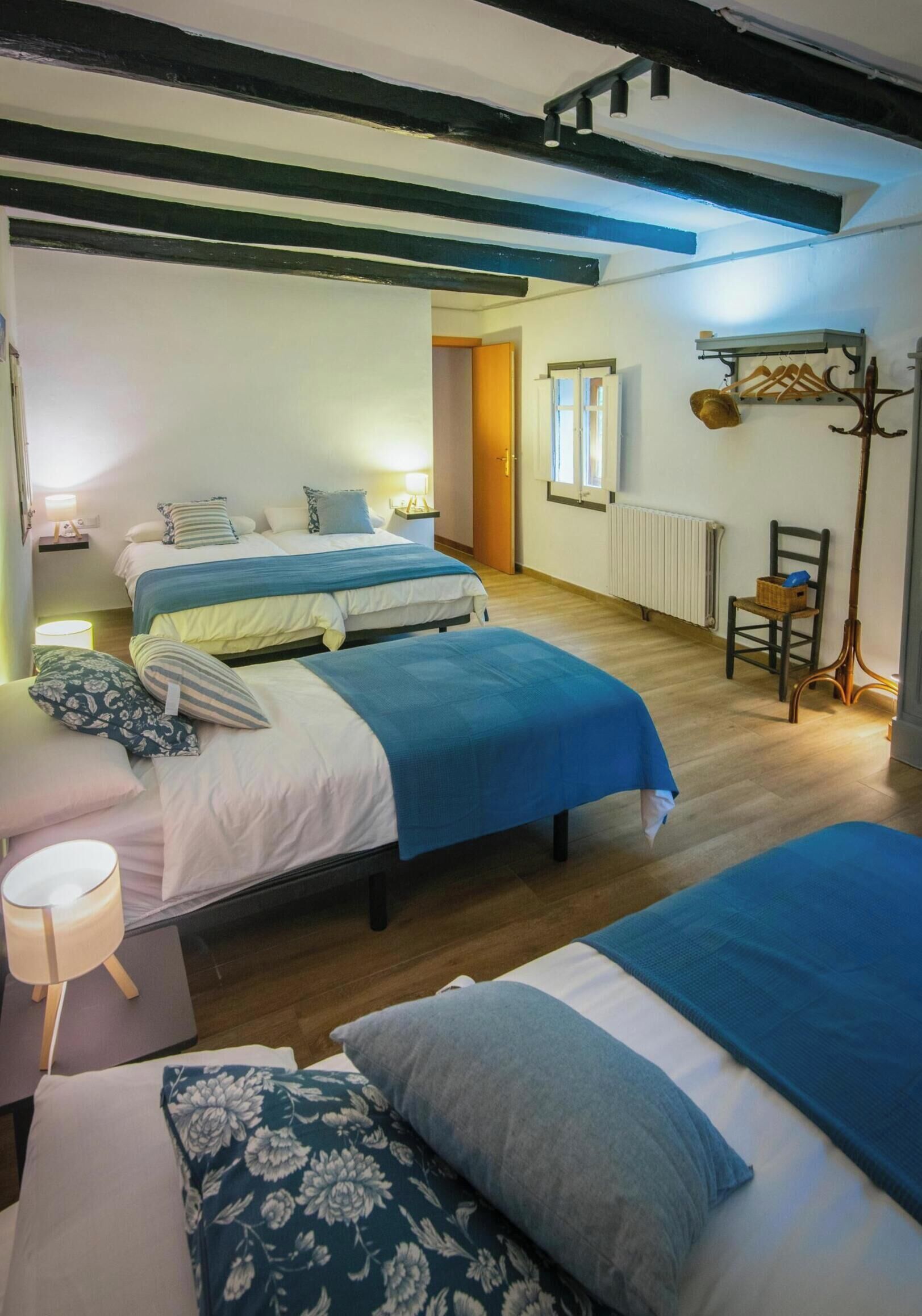 Una habitación con dos camas, una silla, una lámpara y una guitarra.