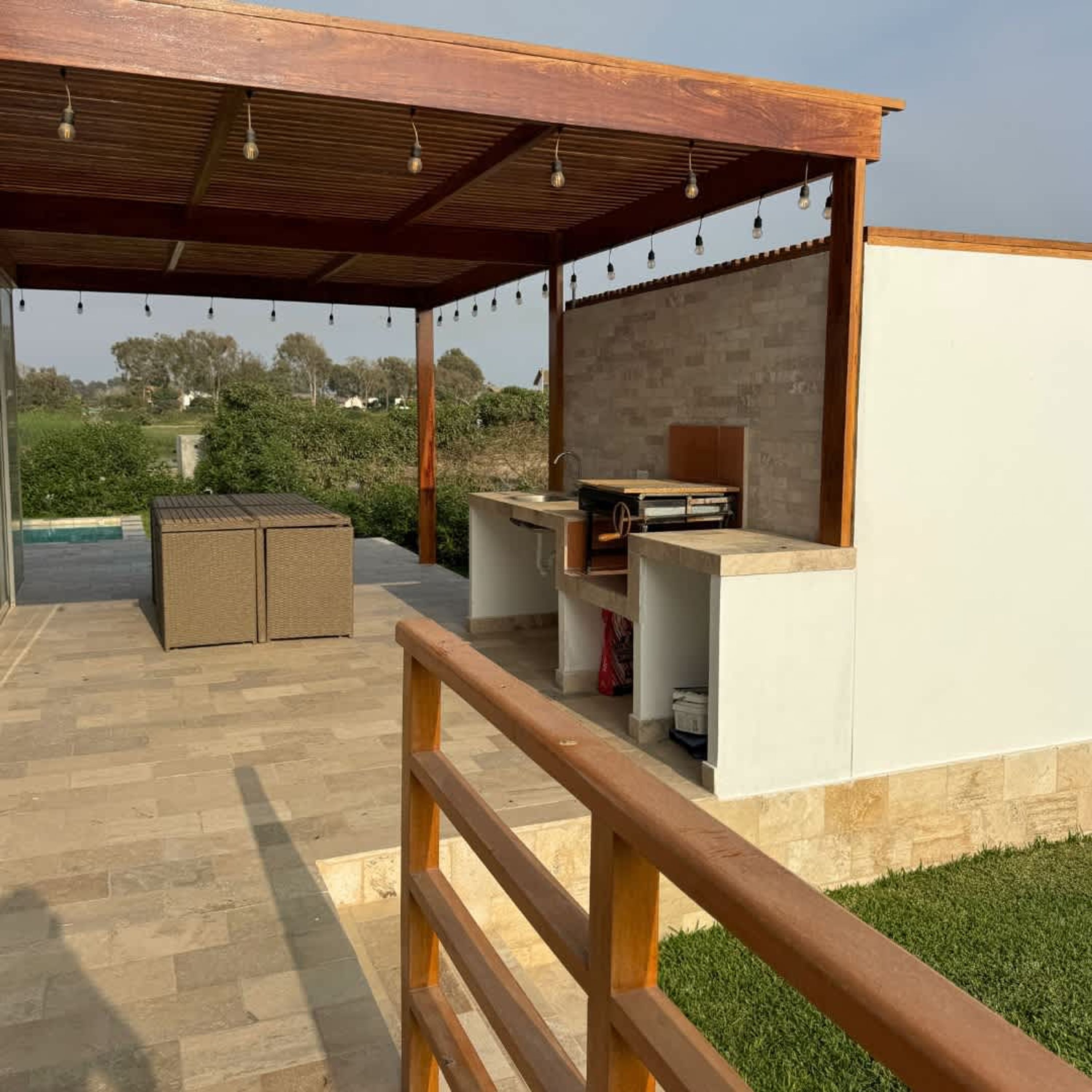 An outdoor patio with a wooden pergola, a built-in grill station, and a seating area.