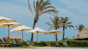 A poolside area with lounge chairs and umbrellas, palm trees, and a clear sky. - HOP Maldivas Elegancia y Tranquilidad Junto a la Laguna (El Carmen)