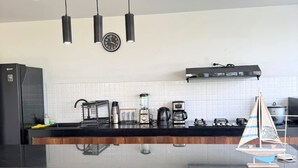 A modern kitchen with a black countertop, white backsplash, and a wooden panel at the bottom. There are three pendant lights, a clock, and a small sailboat model on the counter. - HOP Maldivas Elegancia y Tranquilidad Junto a la Laguna (El Carmen)