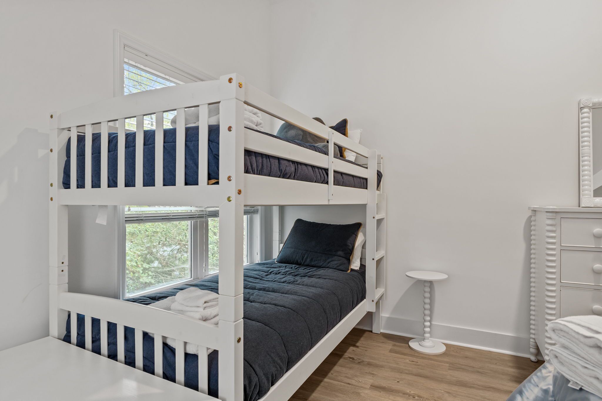 A bunk bed with a window, a small round table, and a dresser with drawers.