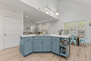 Een moderne keuken met een blauw eiland, witte aanrechtbladen en turquoise stoelen.